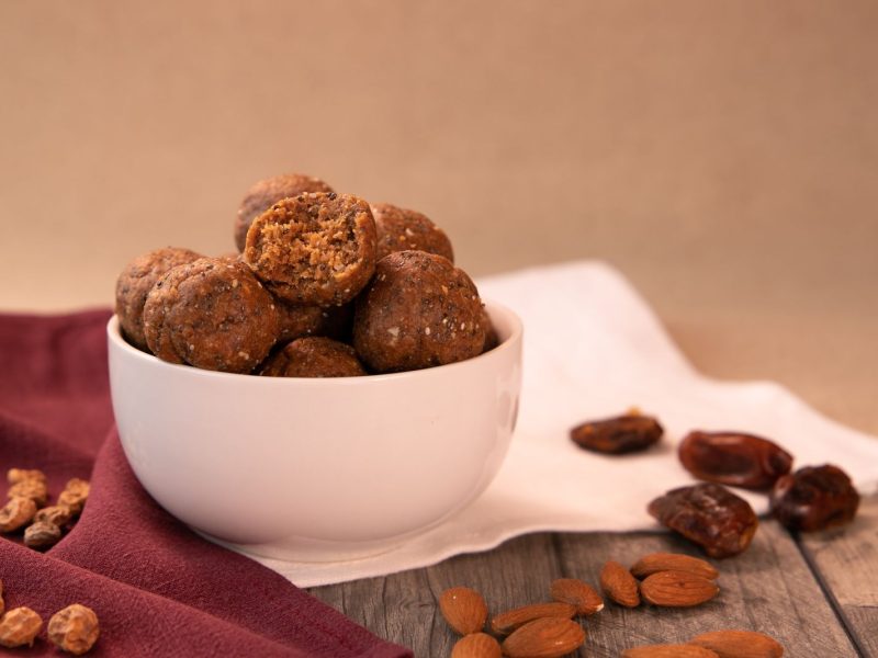 Bolinhas de tâmara e frutos secos numa taça, com tâmaras e amêndoas ao lado