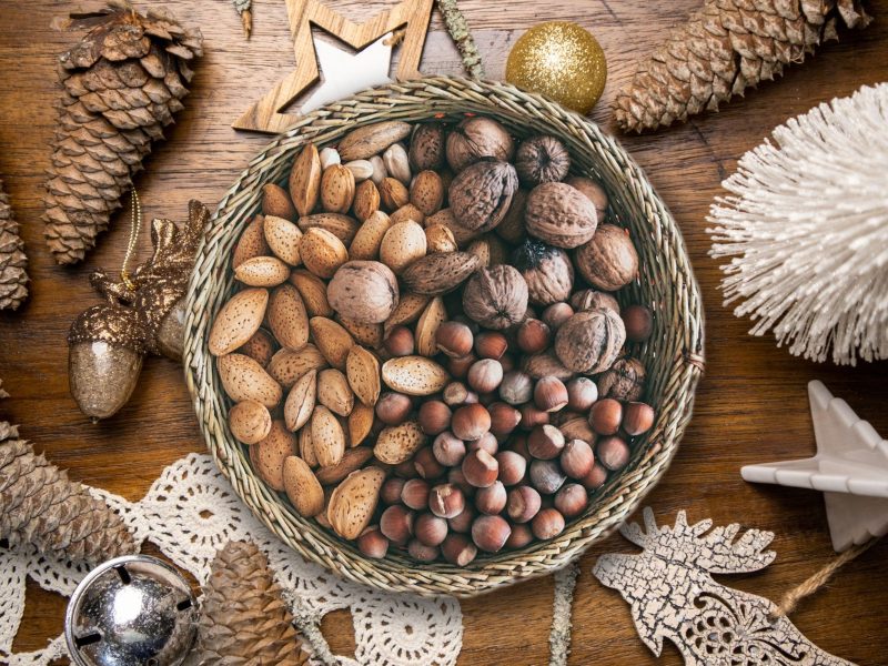 Cesto de vime com amêndoas, nozes e avelãs sobre uma mesa de madeira com decoração de Natal: pinhas, estrela e bolas douradas