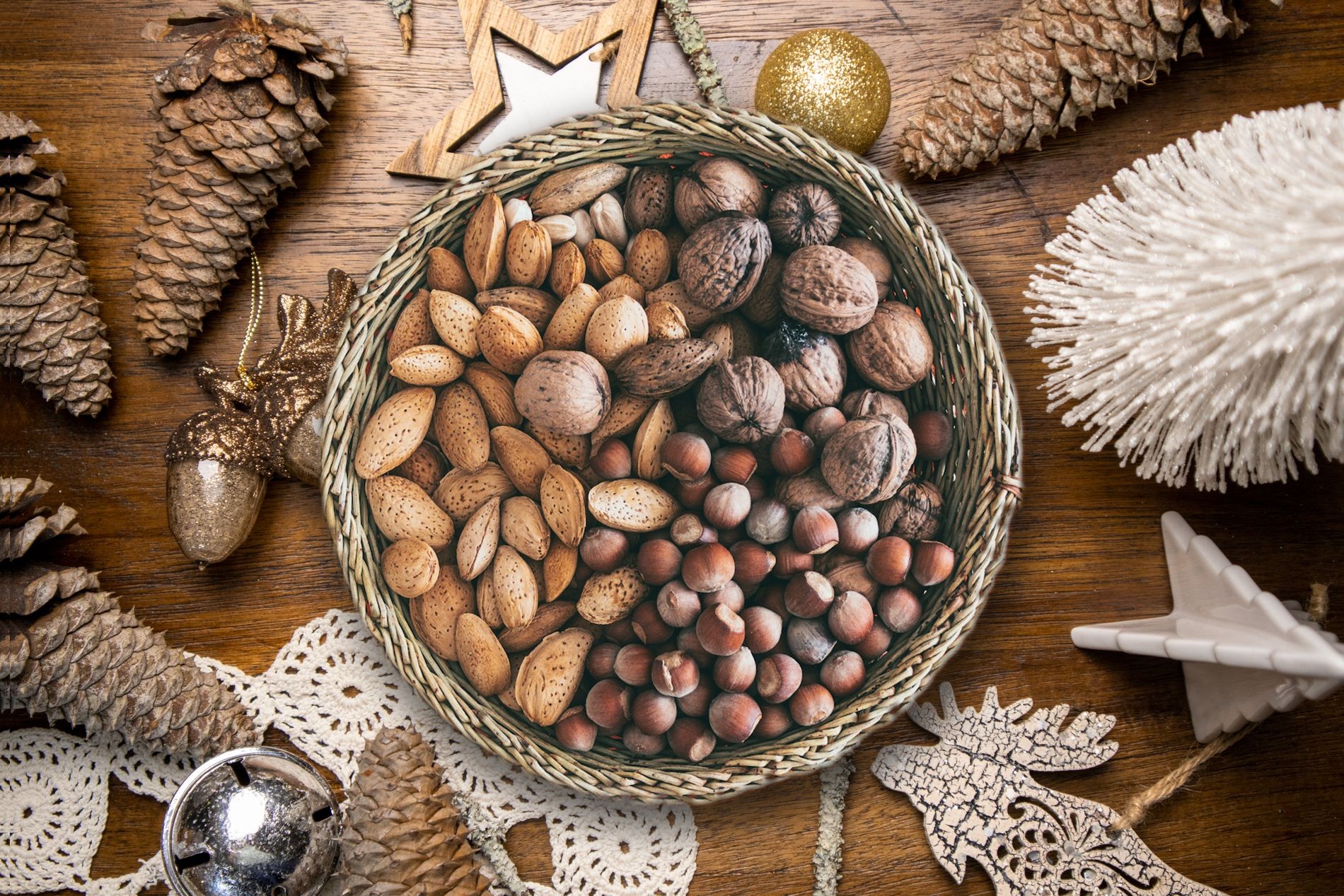 Cesto de vime com amêndoas, nozes e avelãs sobre uma mesa de madeira com decoração de Natal: pinhas, estrela e bolas douradas